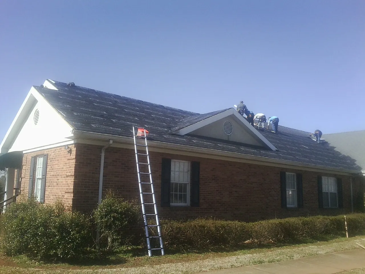 Crew tearing shingles off a brick ranch roof with a ladder set — Metal Roof Repair work by our crew in Hamilton